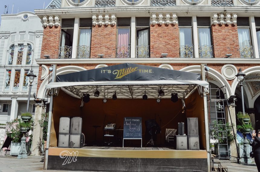 Palco de música ao ar livre montado diante de uma fachada histórica ricamente detalhada.
