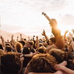 Público reunido em um festival de música ao ar livre durante o pôr do sol.