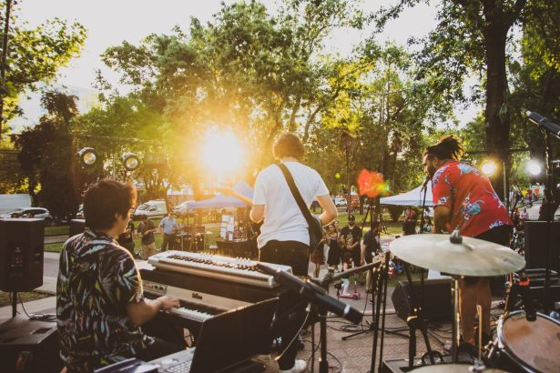 Músicos se apresentam em um palco ao ar livre durante o pôr do sol, diante do público.