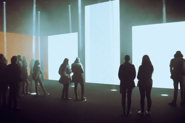 Visitantes observam uma exposição de arte digital imersiva com grandes telas iluminadas.