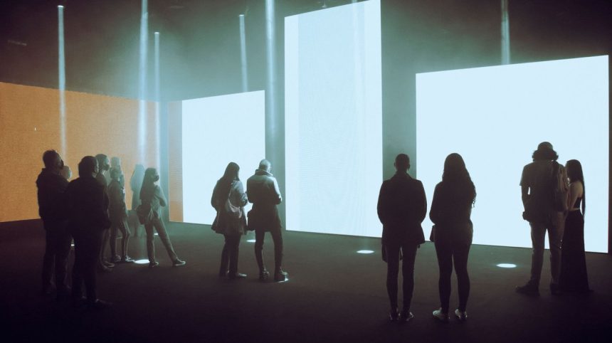 Visitantes observam uma exposição de arte digital imersiva com grandes telas iluminadas.