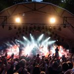 Banda se apresenta em palco ao ar livre diante de um público entusiasmado durante um festival de música.