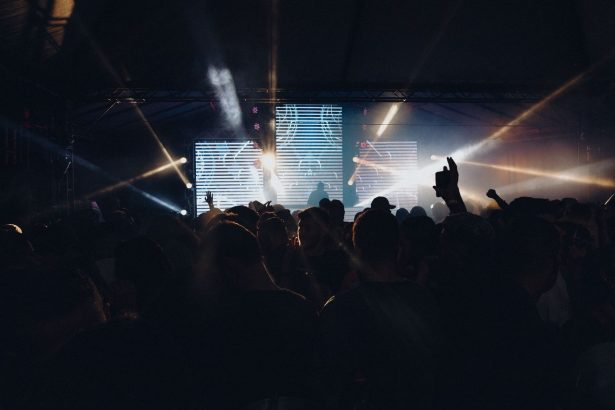 Público acompanha um show noturno ao ar livre, diante de um palco iluminado.