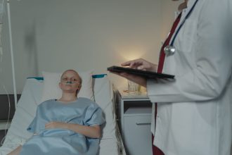 Paciente em leito hospitalar enquanto uma profissional de saúde consulta um tablet ao seu lado.