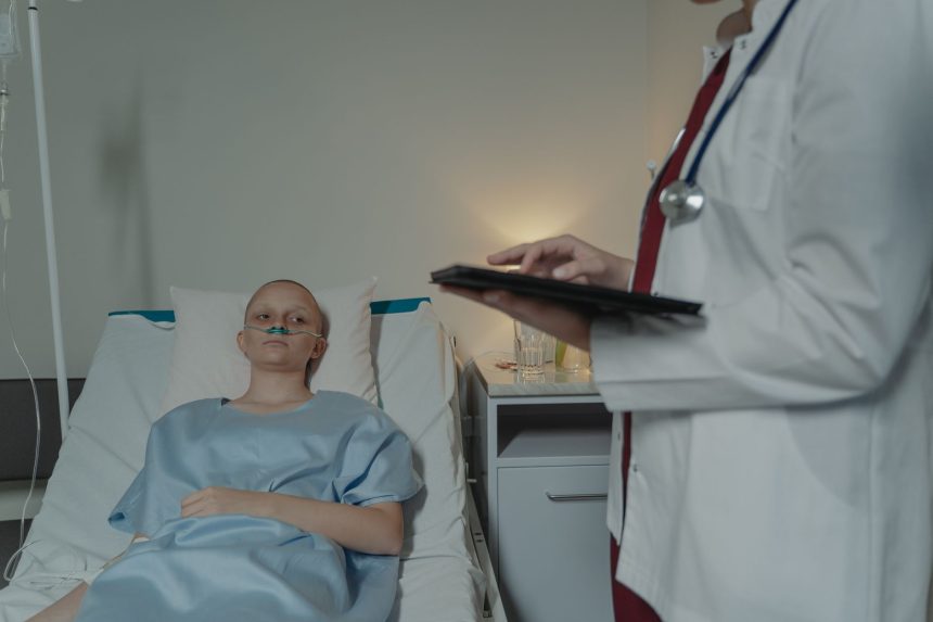 Paciente em leito hospitalar enquanto uma profissional de saúde consulta um tablet ao seu lado.