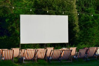 Espaço de cinema ao ar livre, com cadeiras listradas diante de uma tela em branco, cercado por vegetação.