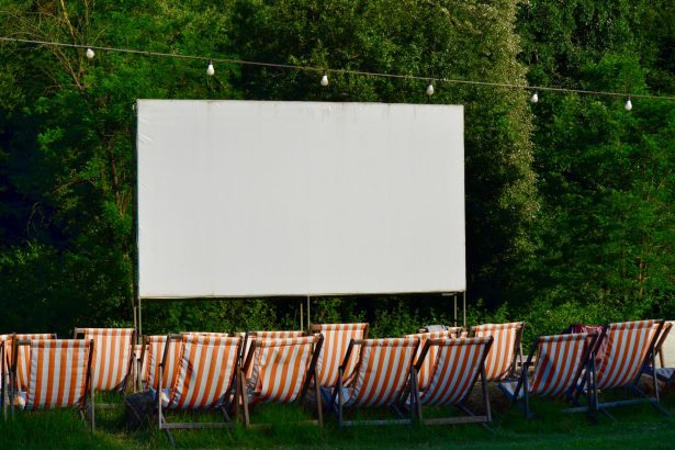 Espaço de cinema ao ar livre, com cadeiras listradas diante de uma tela em branco, cercado por vegetação.