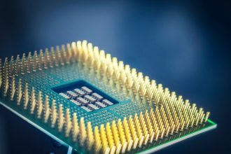 Close de um chip de computador com pinos dourados sobre fundo azul.